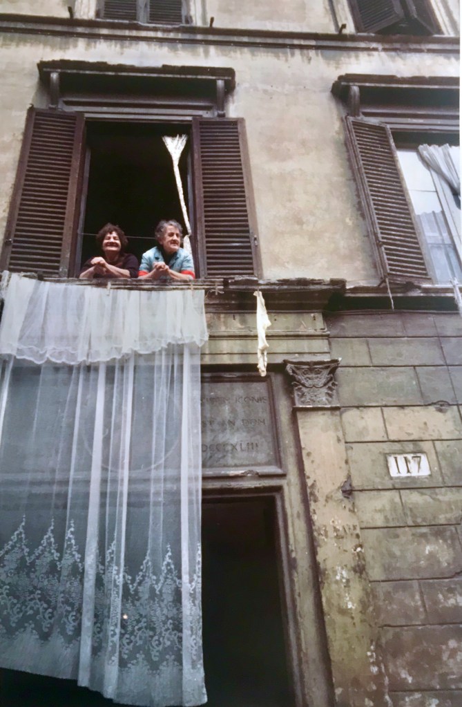 Two Italian women in the former Palazzo Scanderbeg survey the activity below while airing out their exquisite draperies.